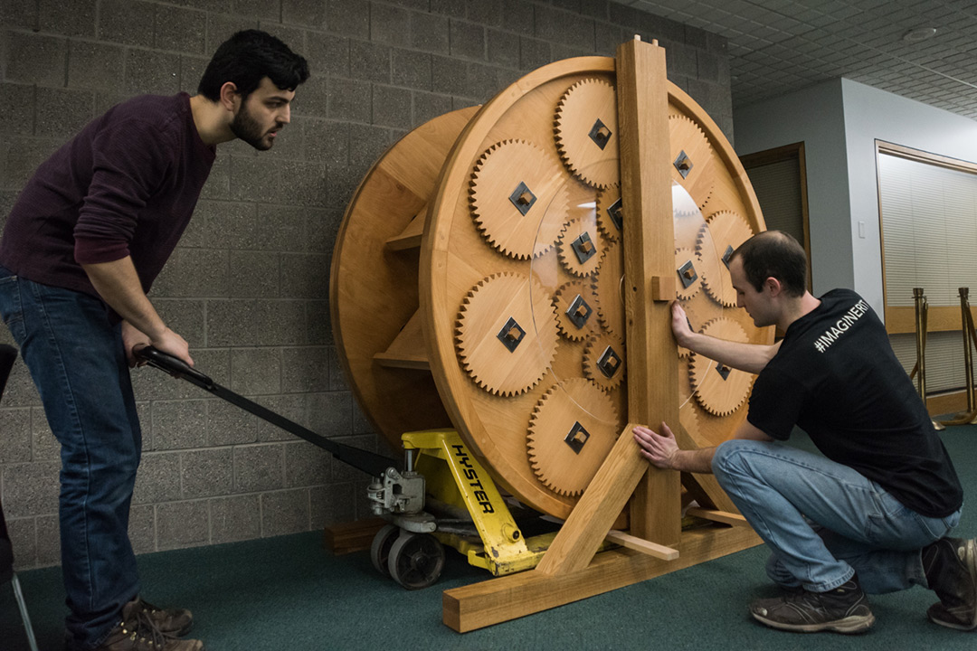Two students set large wooden wheel with medium and small-sized gears on floor