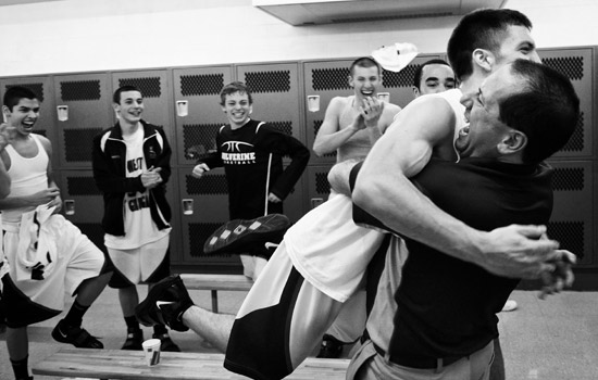 black and white photo of a basketball coach hugging a player in a locker room.