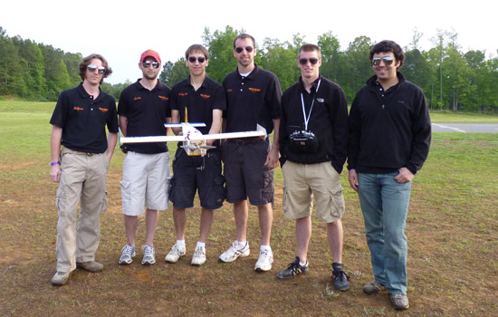 group of six college students holding a model airplane.