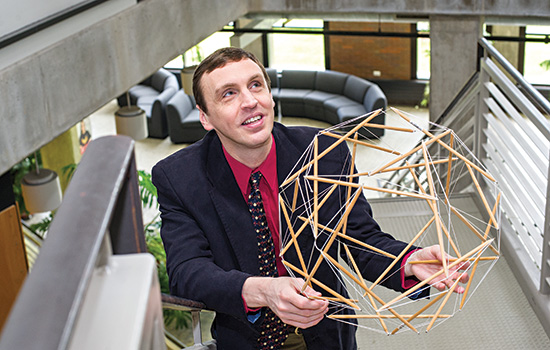 professor holding a round structure of sticks and strings.
