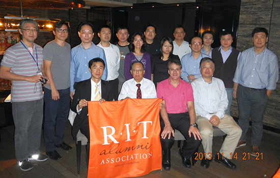 group of people in a restaurant holding an R I T alumni banner.