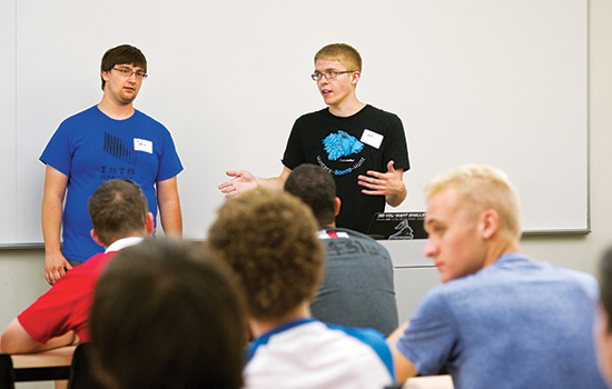  two people talking to a group of people in class.