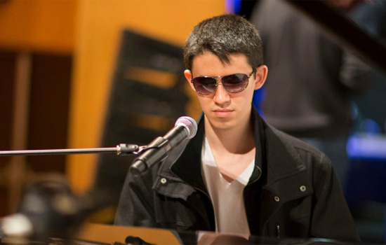 pianist Justin Kauflin wearing glasses with a microphone in front of him.