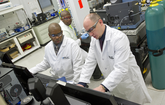 three people in white coats and googles working in a lab.