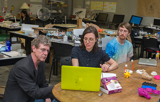 student discusses with professor, both look at laptop screen.