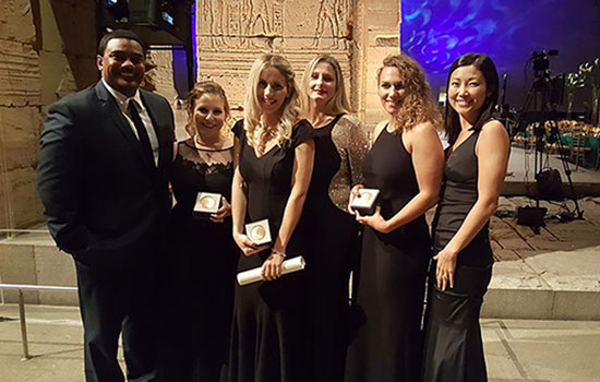 college students wearing formalwear posing outside with awards.