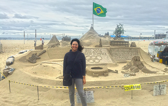 person standing on a beach next to an elaborate sand castle creation.