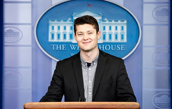 Portrait of Tom Brenner standing in front of the white house logo in the briefing room.