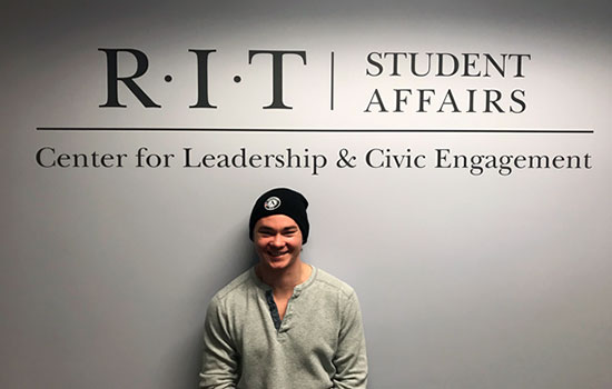 Dan Grinthal poses in front of student affairs wall.