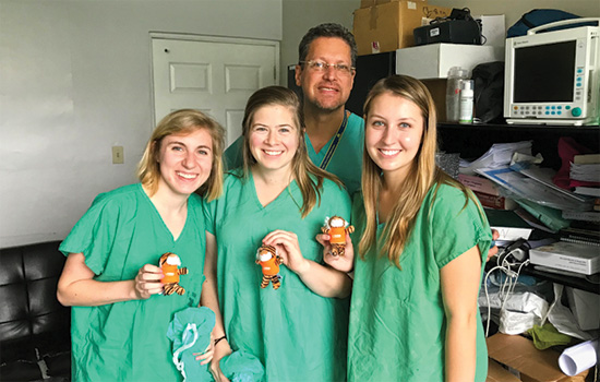 4 people in green lab wear showing off miniatures