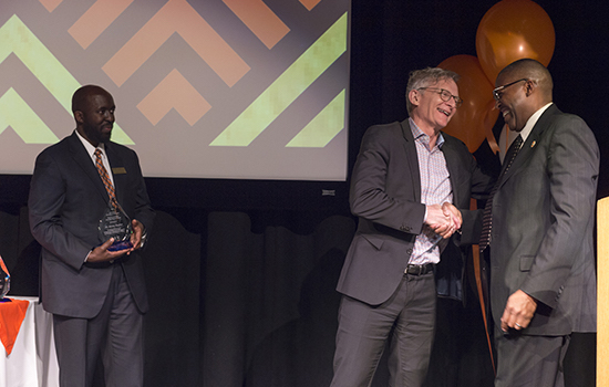 two people shaking hands while third person holds award to the left.