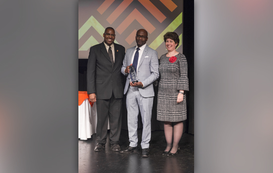 three people pose for photo, person in middle holding award.