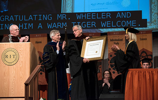  speaker receives honorary degree on stage while others clap.