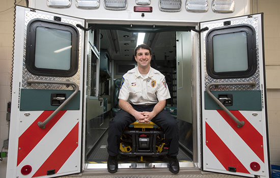  person in uniform sitting in the back of an ambulance smiling.