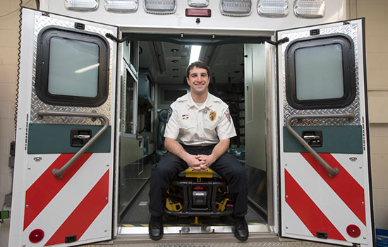 person in uniform sitting in the back of an ambulance smiling.