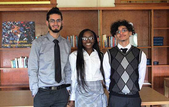 three students dressed up pose for a group photo in front of book cases.