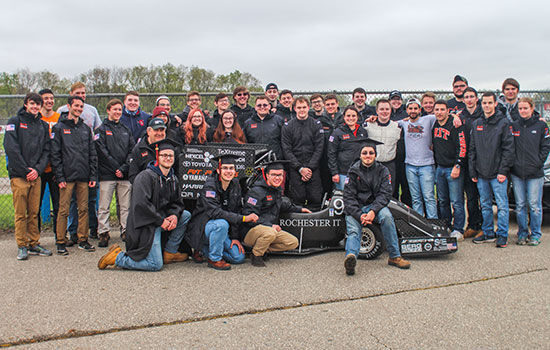 team picture in front of car with graduates wearing their caps.