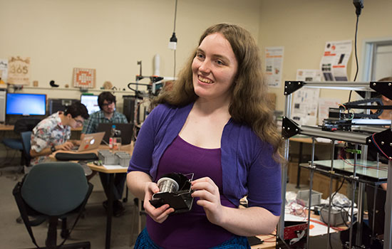 student wearing purple top and holding materials in lab.