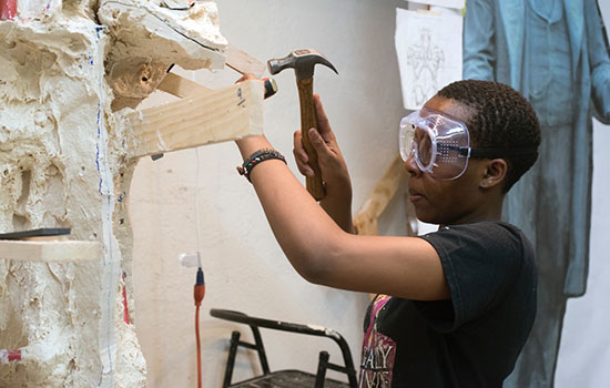 student hammering and wearing safety goggles.