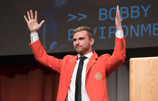  student with hands in the air wearing an orange jacket.