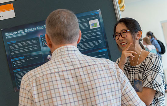 student presents research to person with poster.