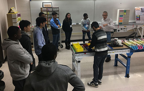 group of students circle around table where one is building something.