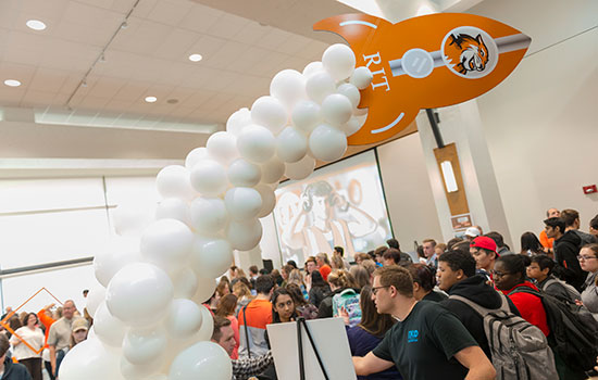  Rit rocketship trailed by white balloons in the fireside lounge with students around.