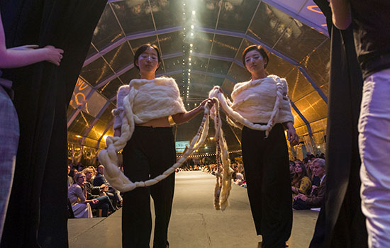 two people holding and wearing fashion pieces during show. Sweaters are heavily knit.