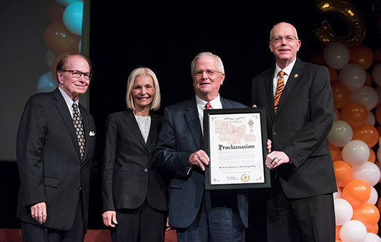 Three people hold certificate next to president Munson on stage.