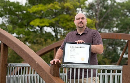 man posing on a bridge with his degree.