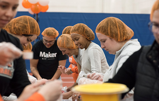 people in orange hair nets prepping meals.