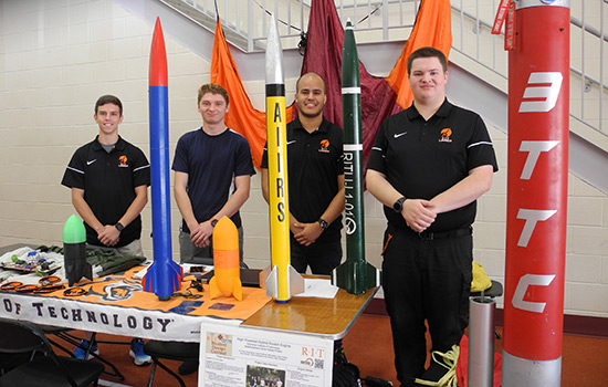 RIT launch initiative poses for picture at table with rockets.